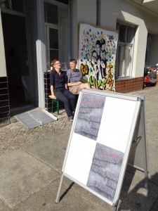 two people sitting outside the gallery on a bench in the sun
