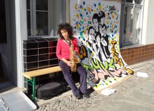 layla sitting on a bench outside the gallery with a sax in their hand, nxt to grafitti by nancy rhode